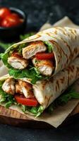 Fresh grilled chicken wraps with lettuce and tomato served on a wooden board with a dark background photo