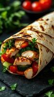 Delicious chicken wrap filled with fresh vegetables served on a dark stone surface photo