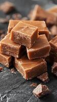 Creamy fudge pieces stacked on a dark slate surface with crumbs scattered around in a cozy kitchen setting photo