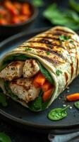 Grilled chicken wrap with fresh spinach and roasted carrots served on a black plate photo
