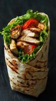 Grilled chicken wrap with fresh lettuce and tomatoes served on a dark background photo