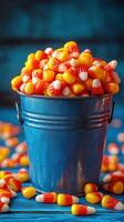 Bright bucket filled with candy corn surrounded by scattered pieces on a vibrant blue background photo