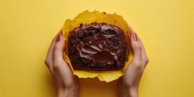 Chocolate cake held in hands against a bright yellow background perfect for celebrations or desserts photo