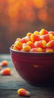 Colorful candy corn fills a deep red bowl set against a blurred autumn background, creating a festive seasonal atmosphere for fall celebrations photo
