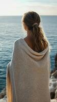 Woman wrapped in a blanket overlooking the serene sea at sunset, enjoying the moment of tranquility and reflection photo