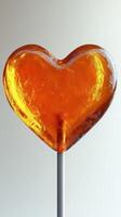 Heart-shaped candy on a stick with a vibrant orange hue, perfect for celebrations and sweet treats photo