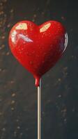 Lollipop shaped like a heart with vibrant red color and glossy finish against a dark background photo