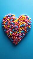 Colorful heart shape made from assorted candy on a blue background displaying sweetness and joy photo
