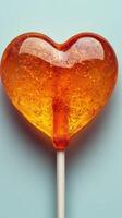 Heart-shaped lollipop in vibrant orange color against a light blue background photo