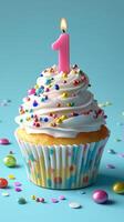 Colorful first birthday cupcake with a candle and sprinkles on a blue background photo