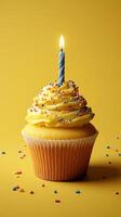 Celebration cupcake topped with frosting and a lit candle on a bright yellow background photo