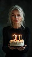 Woman holding a birthday cake with lit candles in a dimly lit setting celebrating a special occasion photo