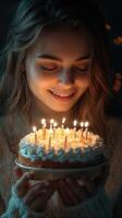 Young woman smiles joyfully while holding a beautifully decorated birthday cake with lit candles in a dimly lit room photo