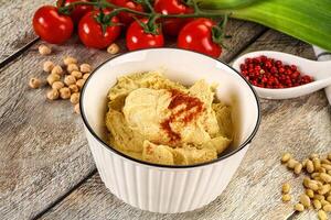 A bowl of hummus with a spoon and a tomato photo