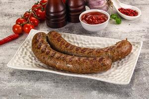 Two sausages on a white plate with tomatoes and ketchup photo