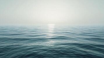 The ocean is calm and peaceful, with the sun setting in the background. The water is a deep blue color, and the sky is a light gray. The scene is serene and tranquil, with no signs of life or activity photo