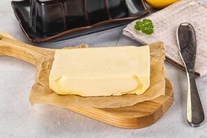 A piece of butter sits on a cutting board next to a knife and a lemon photo