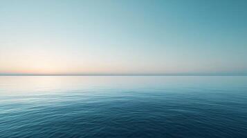 The ocean is calm and peaceful, with a beautiful blue sky in the background. The water is still and the sun is setting, creating a serene atmosphere photo