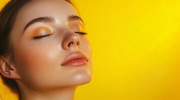 Close-up of a woman with striking makeup, bathed in warm light, showcasing her flawless skin against a bright yellow background. photo