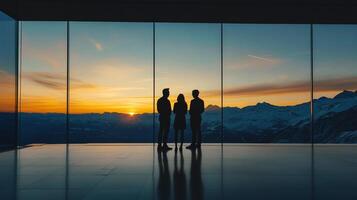 Silhouette of three people in suits at sunset discussing business strategy with a beautiful mountain range in the background. photo