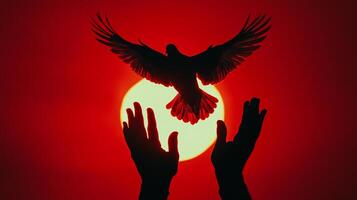Silhouette of a bird taking flight against a vibrant red sky, hands reaching up in the foreground, backlit by a bright, golden sun. photo