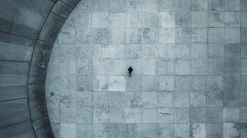 Aerial view of a lone figure walking across a vast concrete plaza, creating a stark and minimalist scene emphasizing solitude and scale. photo