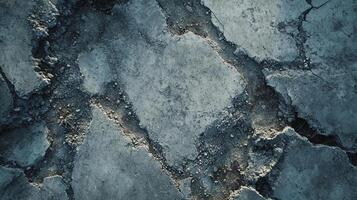 Cracked concrete surface with visible wear and tear, showcasing texture and pattern in shades of gray and blue, implying decay and damage. photo