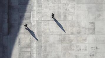 Overhead shot of two anonymous figures walking along a concrete surface, their shadows stretching beside them, creating contrast. photo