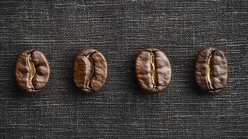 Four coffee beans aligned on dark fabric create a visually appealing contrast, showcasing texture and richness in a minimalistic composition. photo