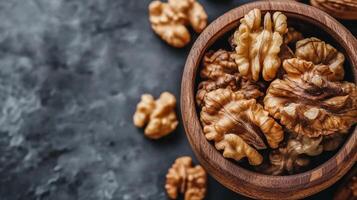 Wooden bowl filled with nutritious walnut halves on a textured surface. Close-up shot, highlighting the kernels' texture. photo