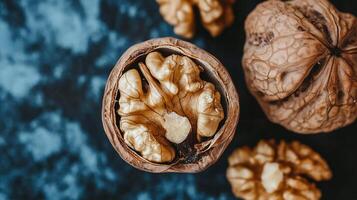 Walnut kernel in half shell, other whole walnuts around. Macro photo of natural food against a blue gray textured background.