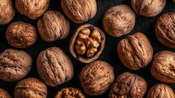 Delicious whole walnuts in their shells, some cracked open, revealing the kernel, presented on a rustic dark surface, inviting snacking. photo