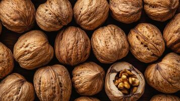 Overhead shot displaying a collection of whole walnuts, one cracked open to reveal the edible kernel inside, on a dark surface. photo