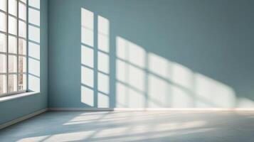 Sunlight streams through a window into an empty room with light blue walls and a concrete floor, creating a pattern of light and shadow. photo