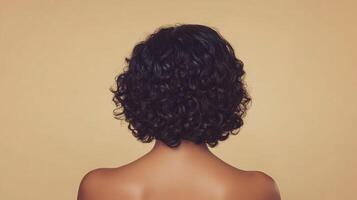 Back view showcases elegant dark, curly hair against a neutral backdrop, emphasizing style and texture. Simple yet sophisticated image. photo
