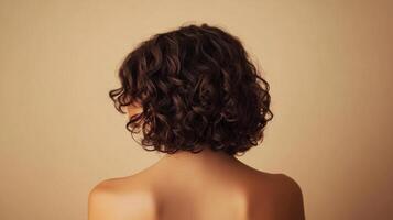 Back view of a person with short, dark, curly hair against a tan background. The focus is on the hair texture and the person's shoulders. photo