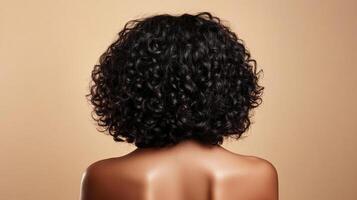 Back of a person with curly dark hair, against a simple light brown background in a studio. Showing smooth shoulders and back. photo