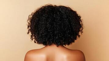 A view from behind showcases a person with a voluminous head of tight, dark, natural curls set against a neutral backdrop. photo