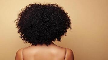 Back view of a woman with voluminous natural hair, showcasing texture and style against a neutral backdrop. Ideal for hair care concepts. photo
