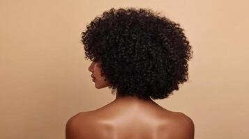 A side-profile shot of a person with curly hair against a cream-colored background, shoulders exposed, head centered in frame. photo