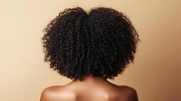 Back view of person with natural, dark, curly hair, showing texture and volume. Beauty and self care concepts. Neutral studio background. photo