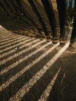 Sunlight reflecting off polished metal tubes casts intricate shadows onto a gravel surface, forming abstract pattern of contrasting light and dark lines, enhancing the modern design. geometric shadows photo