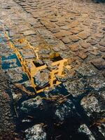 Puddle reflecting building on cobblestone street. Water reflecting building on cobblestone street forms captivating urban landscape, illuminated by warm hues of sunset, creating serene evening scene photo