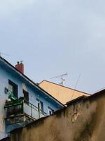Old, colorful, weathered buildings with balconies. Low angle view of weathered buildings with balconies, antennas, and chimneys against a cloudy sky, showcasing urban decay and architectural details photo
