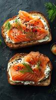 Slices of smoked salmon on toasted bread with cream cheese and herbs displayed on a dark stone surface photo