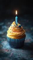 Celebrate with a delicious cupcake featuring a blue candle and colorful sprinkles on a dark, textured background photo