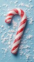 Festive candy cane resting on a blue surface surrounded by snow-like sugar sprinkles photo