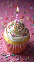 Colorful cupcake with a lit candle surrounded by sprinkles on a pink background for celebrating special occasions photo
