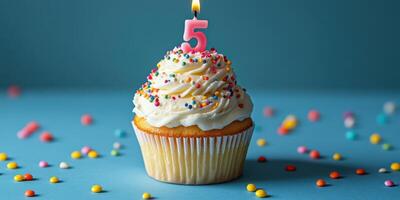 Delicious birthday cupcake with colorful sprinkles and a glowing candle displayed against a bright blue background photo