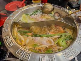 Steaming hot pot filled with vegetables and seafood at a busy diner setting photo